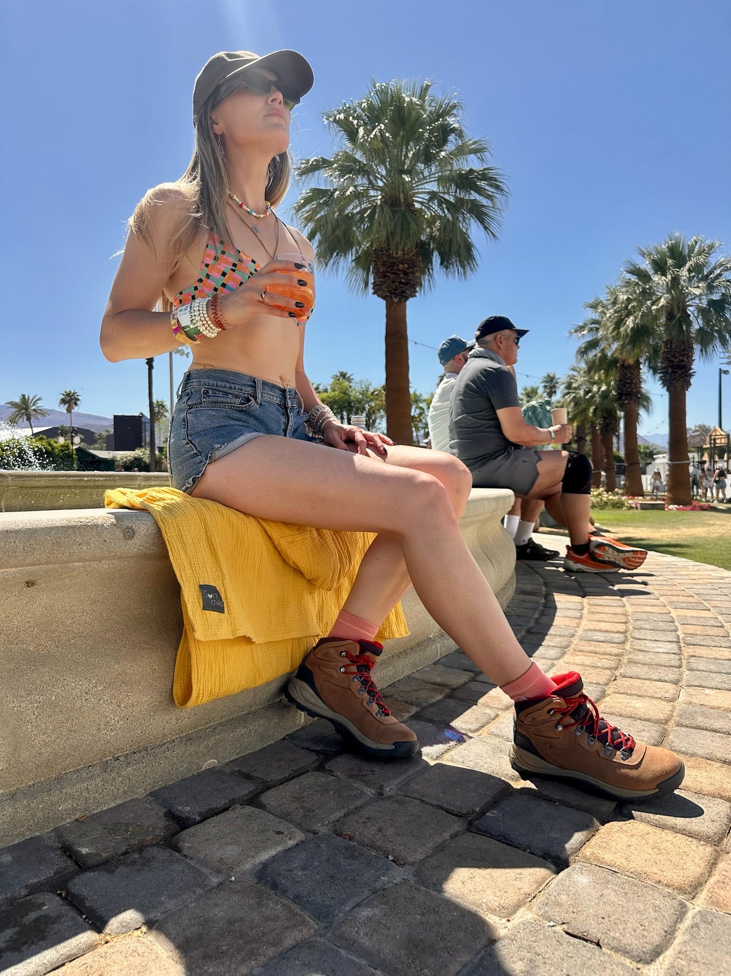 SUNCHILD GOLDEN SLING IMAGE OF NATALIE SITTING AT THE FOUNTAIN AT COACHELLA MUSIC FESTIVAL